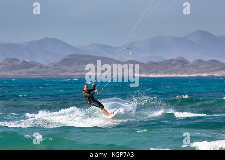 Ein Mann mittleren Alters kite surfs vor der Küste von Corralejo in der Kanarischen Insel Fuerteventura. Lanzarote ist sichtbar im Hintergrund über Isla de L Stockfoto