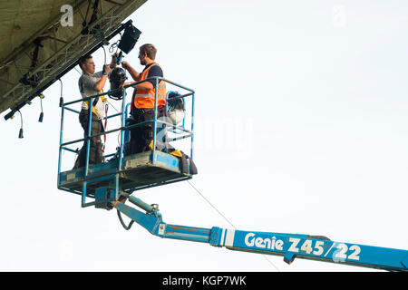 Arbeiten in der Höhe: Zwei Techniker, die in einer Kirschpflückerwaage stehen und die Lichtanlage bei einem Sommermusikfestival in Großbritannien installieren Stockfoto