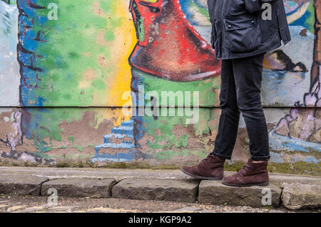 Modell trägt enge schwarze Jeans Skinny Hose und Brown suede Ankle Boots und Wandern vor einer Graffiti-wand. Konzentrieren Sie sich auf die Beine und Schuhe. Stockfoto