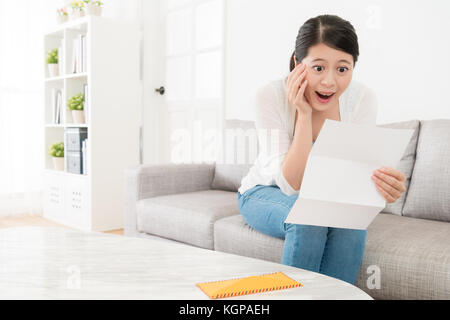 Freundliche hübsche Studentin erhielt die Schule eintritt Benachrichtigungsschreiben Gefühl überrascht, als sie auf dem Sofa zu Hause sitzen. Stockfoto