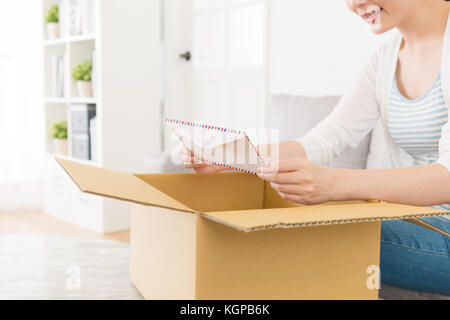 Attraktive junge Dame auspacken Lieferung Paketbox zu Hause und finden Umschlag an Inhalt Suchen bestätigen, die ihr Paket geben. Stockfoto