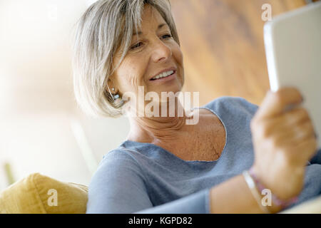 Ältere Frau auf Sofa mit digitalen Tablet angeschlossen Stockfoto