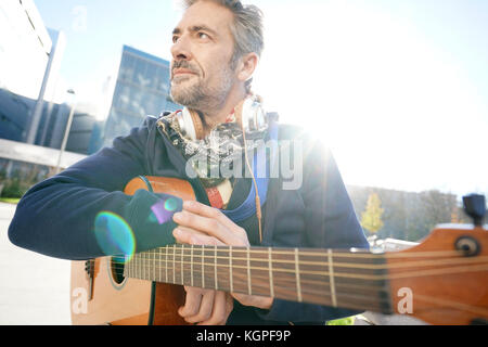 Musiker sitzt auf der Bank mit Gitarre genießt sonnigen Tag Stockfoto