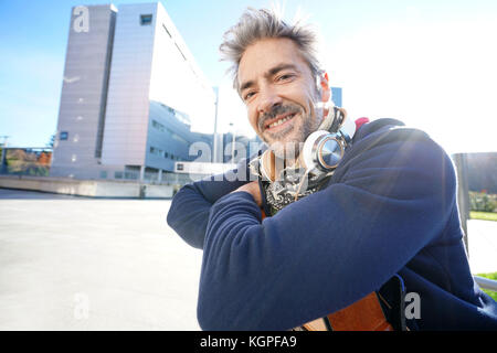 Musiker sitzt auf der Bank mit Gitarre genießt sonnigen Tag Stockfoto