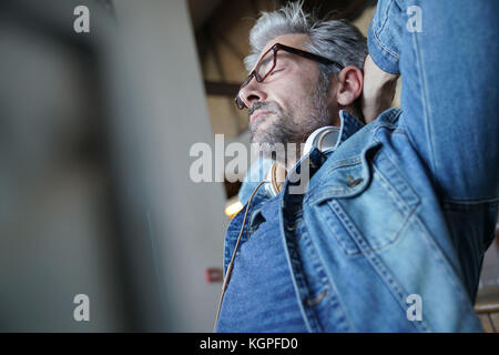 Reifer Mann mit blauen Jeans Jacke stretching Waffen im Stuhl Stockfoto