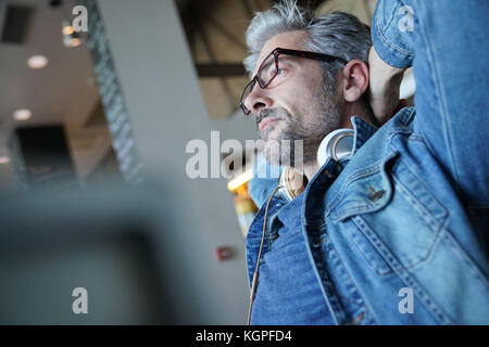 Reifer Mann mit blauen Jeans Jacke stretching Waffen im Stuhl Stockfoto