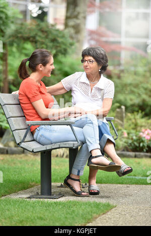 Ältere Frau mit pflegeperson sitzt auf der Bank im Park Stockfoto