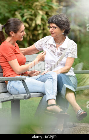 Ältere Frau mit pflegeperson sitzt auf der Bank im Park Stockfoto