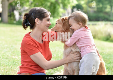 Frau und Baby Mädchen umarmt Golden Retriever Hund Stockfoto