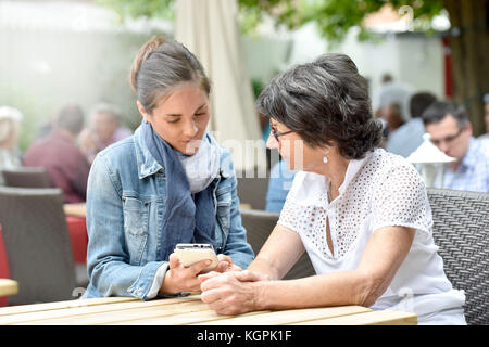 Ältere Frau und Hausfrau auf der Café-Terrasse mit dem Smartphone Stockfoto