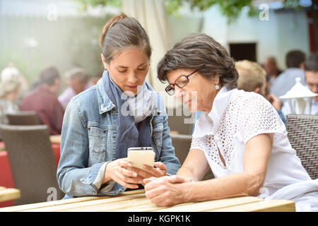 Ältere Frau und Hausfrau auf der Café-Terrasse mit dem Smartphone Stockfoto