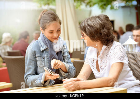 Ältere Frau und Hausfrau auf der Café-Terrasse mit dem Smartphone Stockfoto