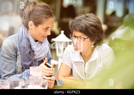 Ältere Frau und Hausfrau auf der Café-Terrasse mit dem Smartphone Stockfoto