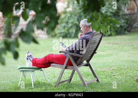 Man relaxen im Liegestuhl und die Verwendung von Tablet Stockfoto