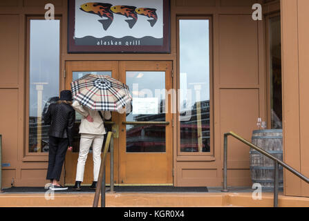 Juneau, Alaska, USA - 28. Juli 2017: Zwei Frauen durch die Scheibe der Eingangstür eines geschlossenen Alaskan Restaurant suchen. Stockfoto