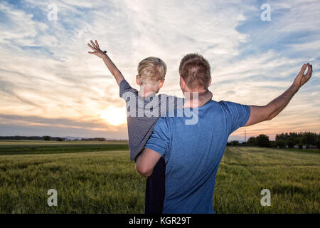 Vater und Sohn in einem offenen Feld bei Sonnenuntergang mit offenen Armen allumfassenden Natur Stockfoto