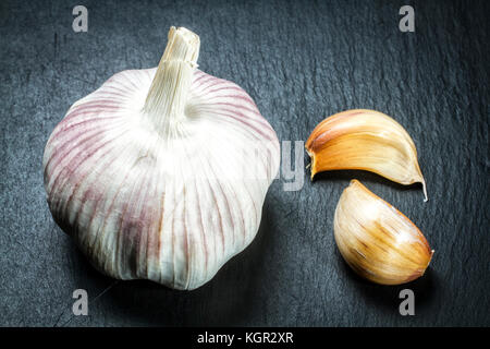 Glühlampe und Nelken Knoblauch (Allium sativum) auf schwarzem Schiefer Oberfläche. Stockfoto