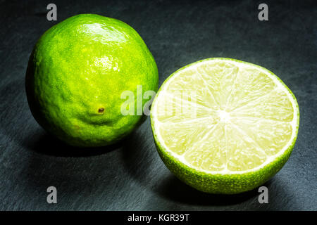 Limette (Citrus aurantifolia) auf schwarzem Schiefer. Stockfoto