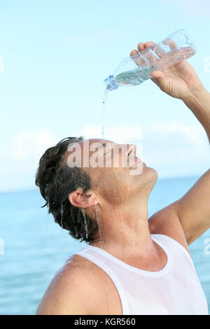 Schöner Mann gießt Wasser aus der Flasche auf seinem Gesicht Stockfoto
