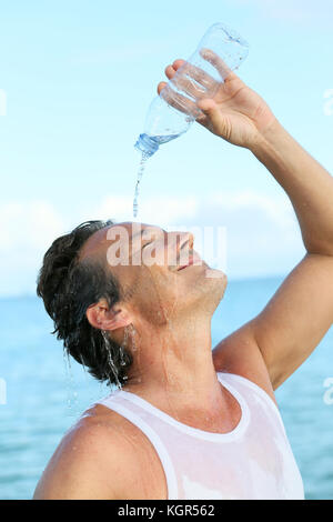 Schöner Mann gießt Wasser aus der Flasche auf seinem Gesicht Stockfoto