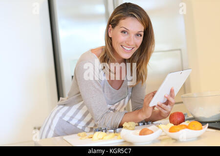 Lächelnde blonde Frau auf Rezept auf digitalen Tablet suchen Stockfoto