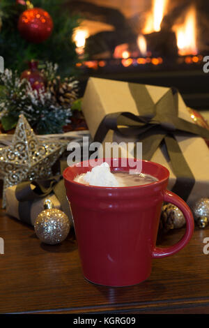 Tasse heiße Schokolade mit Weihnachtsschmuck und Kamin im Hintergrund Stockfoto