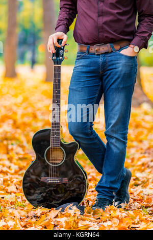 Close up Hände der person Mann auf akustischer Gitarre im Herbst Park. Fokus auf der Gitarre. Stockfoto