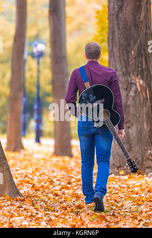 Junger Mann mit akustischer Gitarre zu Fuß auf den Blättern im City Park. Fokus auf der Gitarre. Stockfoto