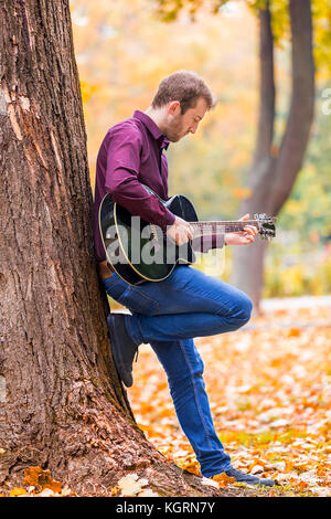 Junge Mann spielt akustische Gitarre im City Park. Fokus auf der Hand. Stockfoto