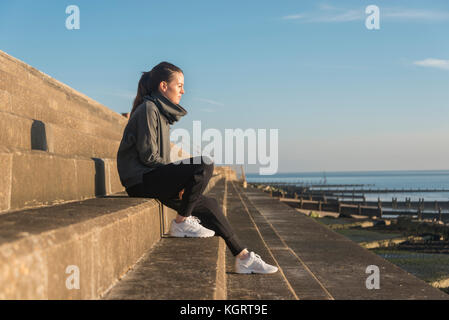 Frau sitzt auf konkrete Schritte neben dem Meer genießen die Nachmittagssonne, nachdenklich. Stockfoto