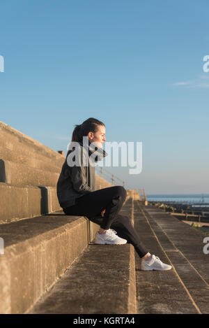 Frau sitzt auf konkrete Schritte neben dem Meer genießen die Nachmittagssonne, nachdenklich. Stockfoto