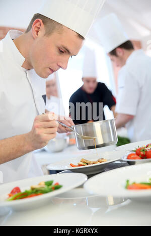 Junge Koch gießen Sauce auf Teller Stockfoto