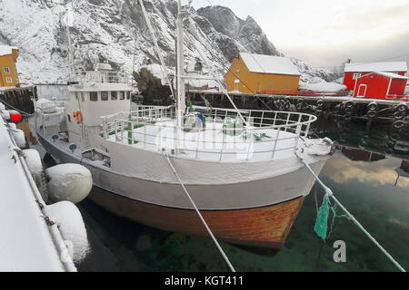 Schnee bedeckt Hafen - Fischerdorf nusfjord - alten hölzernen Fischerboot - bottelvika Bucht - nesheia+sultinden Mounts - Rot + orange Fischerhütten oder Rorbuer fo Stockfoto