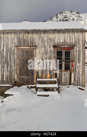 Schnee bedeckt völlig ruiniert - verlassen - Farbe verblasst Holzhütte mit Treppe lehnte sich an der Wand - Fuß des schneebedeckten hustinden neben e10 European Road Mount Stockfoto