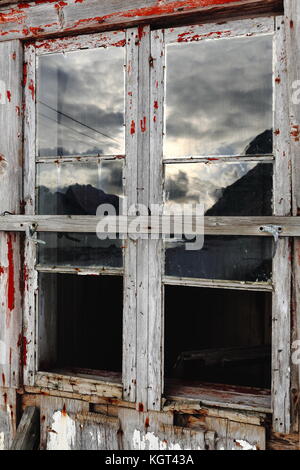 Glas fehlt - gebrochene Fenster von Schnee bedeckt - komplett ruiniert - verlassen - Farbe verblasst Holzhütte am Fuße des schneebedeckten Mount hustinden neben e10 Europea Stockfoto