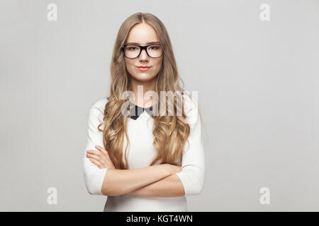 Frau in formale Abnutzung kreuzte die Hände, toothy Lächeln und Kamera. studio Shot, grauer Hintergrund Stockfoto