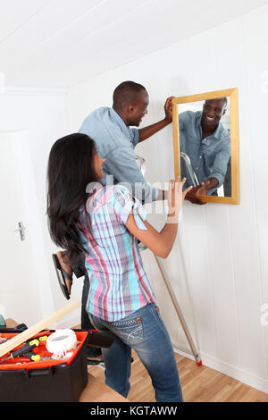 Junges Paar hängenden Spiegel an der Wand Stockfoto