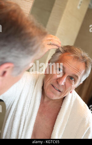 Älterer Mann an Haar im Spiegel zu betrachten Stockfoto