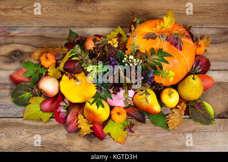 Thanksgiving oder fallen Anordnung mit wilden Blumen in die rosa Vase, Kürbisse, Äpfel, Birnen und buntes Herbstlaub auf dem hölzernen Hintergrund, oben vi. Stockfoto