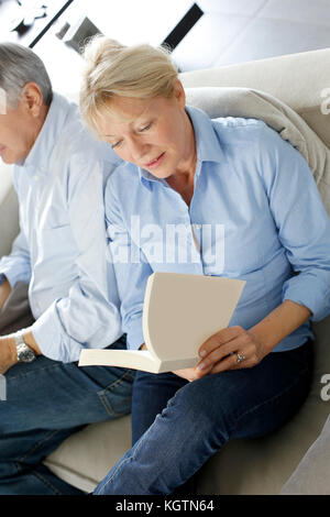 Ältere Frau mit Buch, Mann neben ihr sitzen Stockfoto