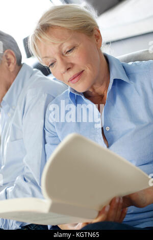 Ältere Frau mit Buch, Mann neben ihr sitzen Stockfoto