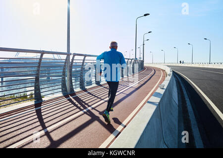 Aktiver Mann, der entlang der Uferbrücke in städtischer Umgebung läuft Stockfoto