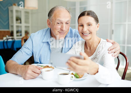 Lächelndes Seniorenpaar macht Selfie am Tisch im Restaurant während des Desserts Stockfoto