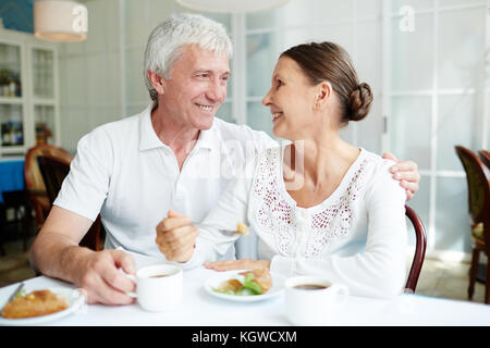 Reifes, liebevolles Paar, das im Café sitzt, Dessert mit Tee oder Kaffee isst und sich unterhalten kann Stockfoto