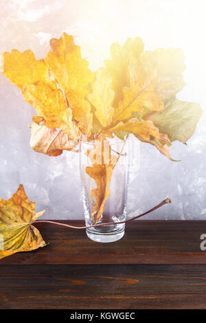 Gelb und Orange Blätter im Herbst in einem Glas auf einem Holzregal Stockfoto