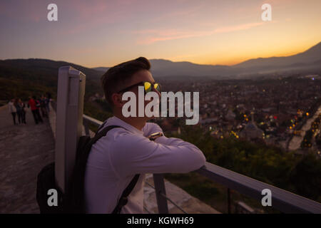 Stilvoll jugendlich mit Sonnenbrille Lean auf Geländer hoch vor der Stadt Prizren, Kosovo im Sonnenuntergang Stimmung Stockfoto