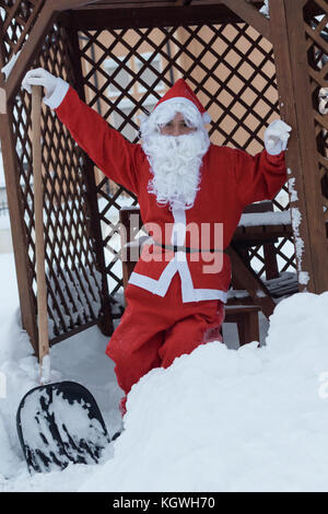 Stolzer weihnachtsmann lehnt sich nach Schneearbeit auf Schaufel Entfernung vor dem Holzhaus Stockfoto