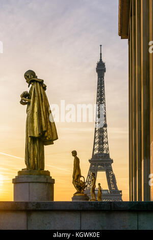 Die aufgehende Sonne beleuchtet die goldenen Statuen auf der Esplanade Trocadero und dem Eiffelturm sich gegen eine orange sky steht. Stockfoto
