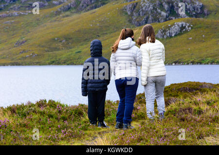 Drei Geschwister (zwei Schwestern und einen Bruder) genießen Sie die Aussicht auf Loch Tollie in Wester Ross, an der Westküste von Schottland und den Atlantischen Ozean Stockfoto