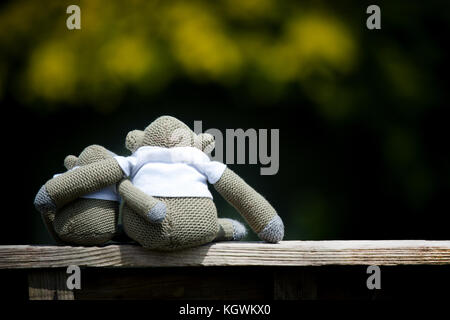 Zwei toy Affen, eine größer als die andere, Sat kuscheln auf einer Holzbank mit ihren Armen um sich gegenseitig Stockfoto